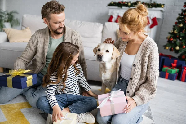 Familie mit Weihnachtsgeschenken streichelt Labrador im heimischen Wohnzimmer — Stockfoto