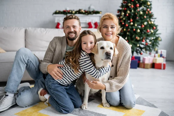 Família feliz com cão labrador olhando para a câmera durante o Natal em casa — Fotografia de Stock