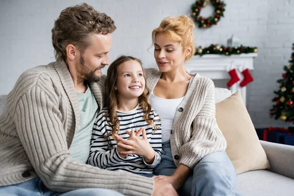 Enfant agréable assis près des parents sur le canapé pendant Noël à la maison — Photo de stock