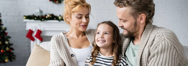 Fröhliches Mädchen, das in der Nähe der Eltern im neuen Jahr im Wohnzimmer wegschaut, Banner — Stockfoto