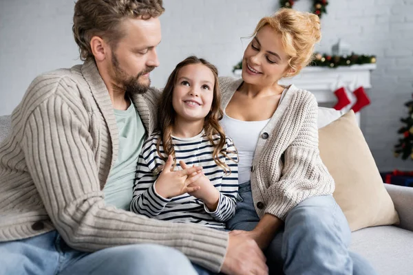 Souriante fille parlant près des parents sur le canapé pendant la nouvelle année à la maison — Photo de stock