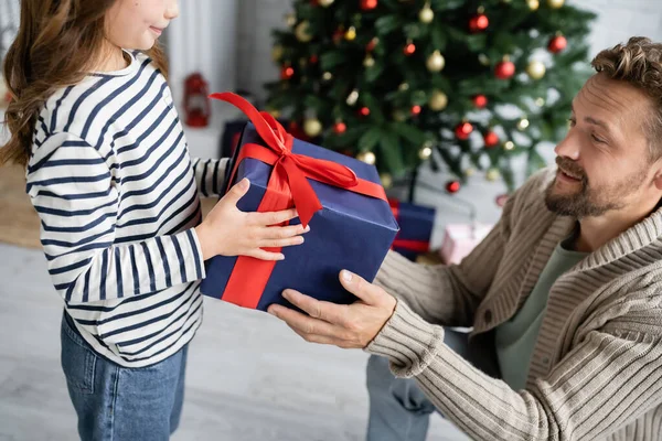 Niño dando regalo de año nuevo a padre cerca borrosa árbol de Navidad en casa - foto de stock