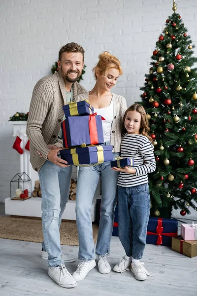 Cheerful family holding gifts near decorated christmas tree in living room — Stock Photo