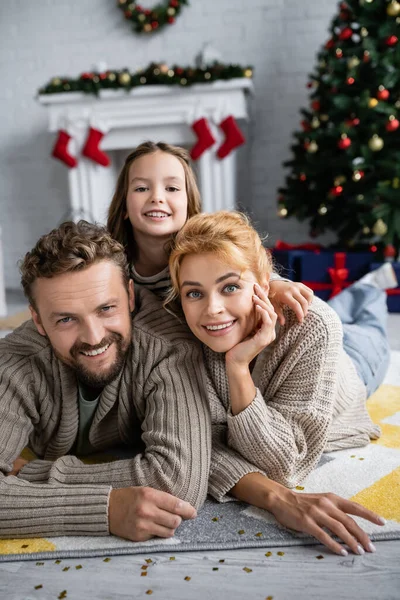 Lächelnde Familie blickt in die Kamera, während sie zu Neujahr mit Konfetti auf dem Boden liegt — Stockfoto