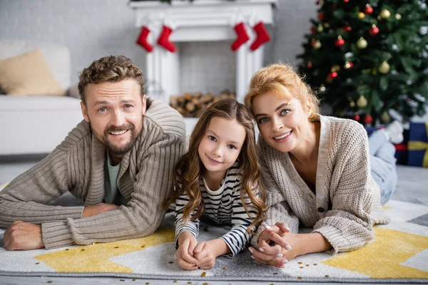 Позитивна сім'я і дитина лежать поруч з конфетті на килимі під час нового року вдома — стокове фото