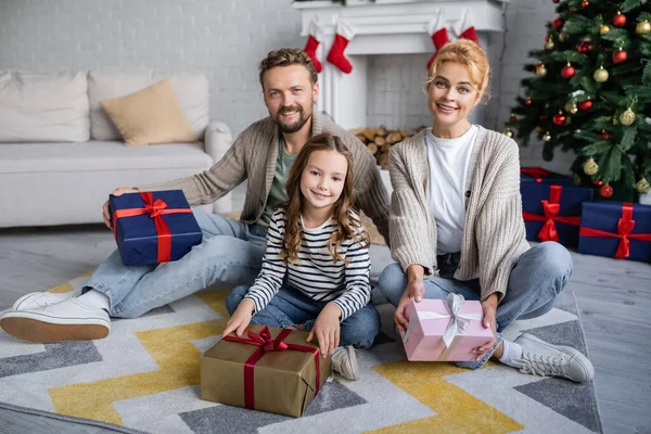 Positive Familie hält zu Hause Neujahrsgeschenke und blickt auf Teppich in die Kamera — Stockfoto