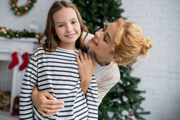 Femme heureuse étreignant et regardant fille lors de la célébration de la nouvelle année à la maison — Photo de stock