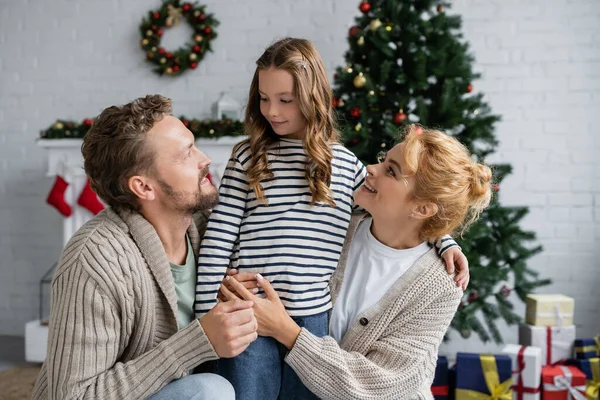 Smiling parents in cardigans looking at daughter during christmas at home — Stock Photo