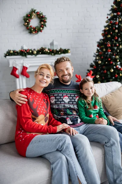 Man in warm sweater hugging daughter and wife on couch at home — Stock Photo