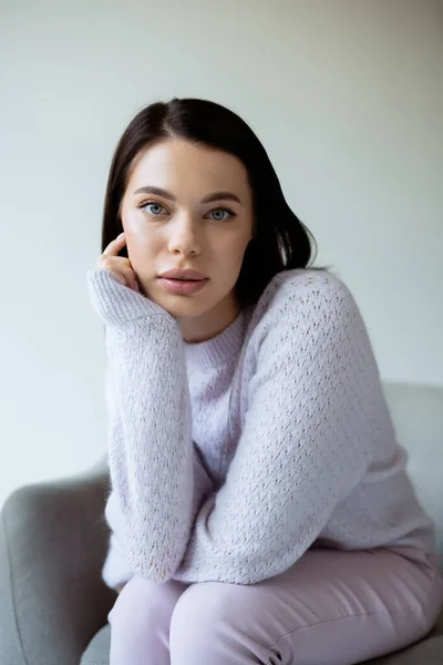 Portrait of brunette woman in soft knitted sweater and natural makeup sitting isolated on grey — Stock Photo