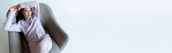 Vista ad alto angolo di elegante donna bruna rilassante in poltrona grigia su sfondo bianco, banner — Foto stock