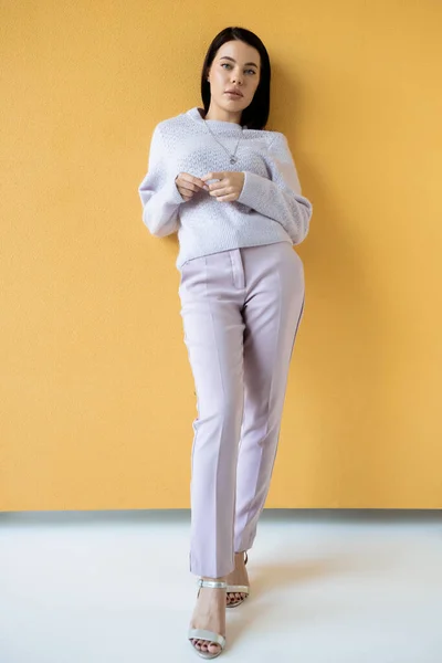 Longitud completa de la mujer morena en ropa elegante y sandalias de pie sobre fondo amarillo - foto de stock