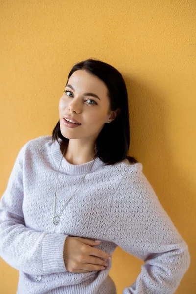 Pleased brunette woman in soft knitted sweater smiling at camera on yellow background — Stock Photo