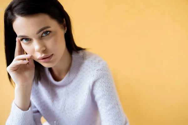 Brunette woman with natural makeup wearing cozy sweater and looking at camera isolated on yellow — Stock Photo