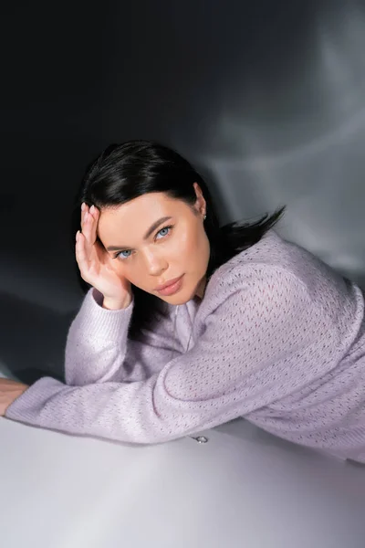 Brunette woman in knitted sweater lying on grey background with lighting — Stock Photo
