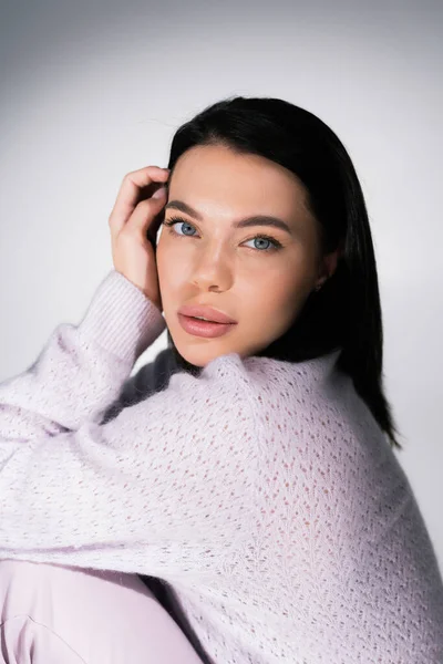 Portrait of young brunette woman in soft sweater and natural makeup looking at camera on grey background — Stock Photo