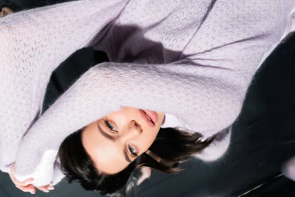 Vista superior da mulher morena bonita em camisola de malha aconchegante deitado no fundo cinza — Fotografia de Stock