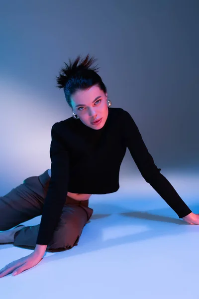 Young brunette woman in black sweater and pants looking at camera while posing on blue background — Stock Photo