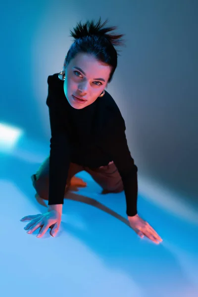 Sensual brunette woman in black sweater looking at camera while posing on blue background — Stock Photo