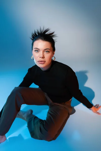 Young brunette woman in black sweater looking at camera while posing on blue background — Stock Photo