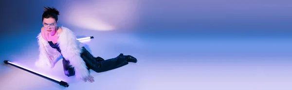 Mujer seductora en pantalones de cuero negro y chaqueta peluda blanca posando cerca de lámparas sobre fondo azul y púrpura, pancarta — Stock Photo
