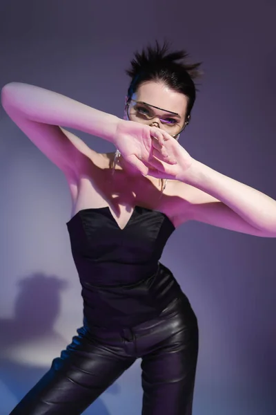 Brunette woman in black corset and leather trousers obscuring face with hands on purple background — Stock Photo