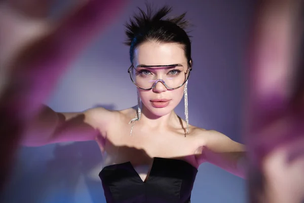 Glamour woman in transparent eyeglasses and black corset looking at camera on blurred purple background — Stock Photo