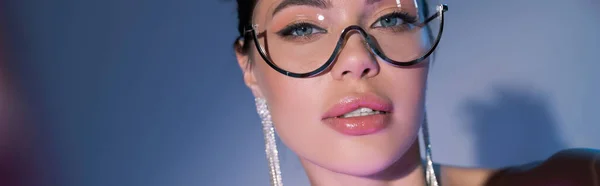 Retrato de mujer bonita en gafas de moda y pendientes brillantes sobre fondo azul, bandera - foto de stock