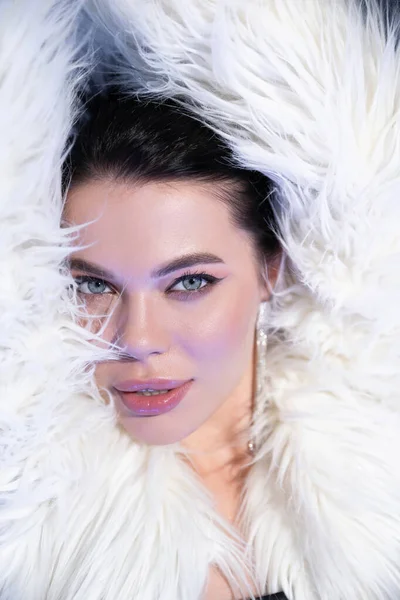 Портрет модной модели в искусственной меховой куртке, позирующей на синем фоне — стоковое фото