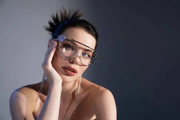Porträt einer stilvollen Frau mit nackten Schultern und Sonnenbrille, die auf grauem Hintergrund in die Kamera blickt — Stockfoto