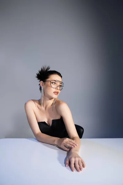 Trendy model in sunglasses and corset posing near table on grey background — Stock Photo