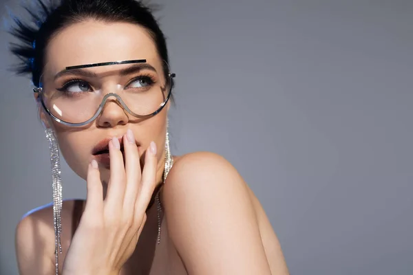 Mujer morena con gafas de sol y pendientes tocando labios aislados en gris - foto de stock