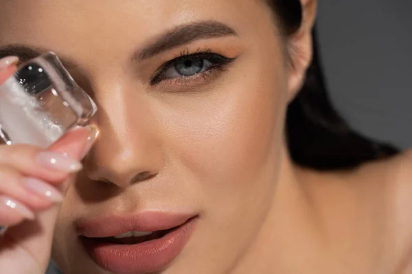 Close up view of brunette woman holding blurred ice cube isolated on grey — Stock Photo