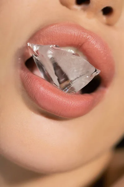 Vista de cerca de la mujer con labios rosados sosteniendo hielo en la boca - foto de stock