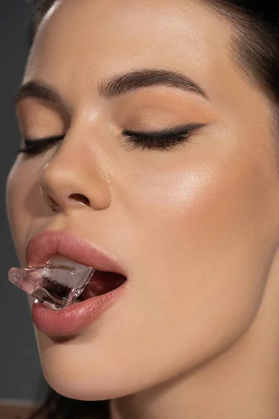 Close up view of young woman with visage holding ice in mouth isolated on grey — Stock Photo