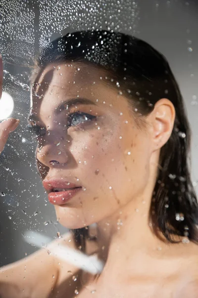 Young brunette woman standing near wet glass on grey background — Stock Photo