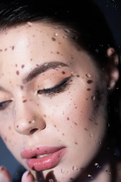 Jeune femme brune avec maquillage regardant loin près de verre humide sur fond gris — Photo de stock