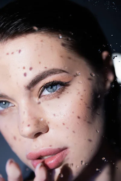 Brunette model with visage touching wet glass on grey background — Stock Photo