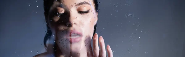 Mujer atractiva mirando y tocando vidrio húmedo sobre fondo gris, bandera — Stock Photo