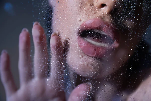 Vista recortada de mujer sexy tocando vidrio con gotas de agua sobre fondo gris - foto de stock