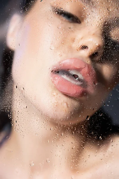 Verschwommene junge Frau mit geöffnetem Mund in der Nähe von nassem Glas auf grauem Hintergrund — Stockfoto