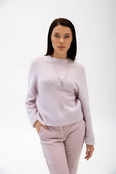 Brünettes Model im warmen Pullover blickt in die Kamera und posiert mit der Hand in der Tasche isoliert auf grau — Stockfoto