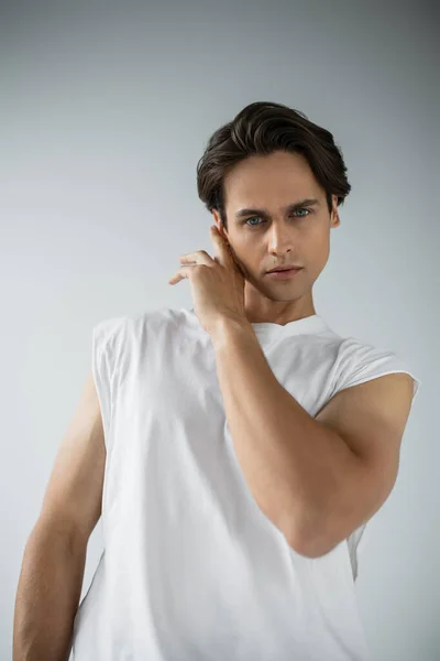 Homme élégant en t-shirt blanc regardant la caméra et toucher le visage sur le gris — Stock Photo