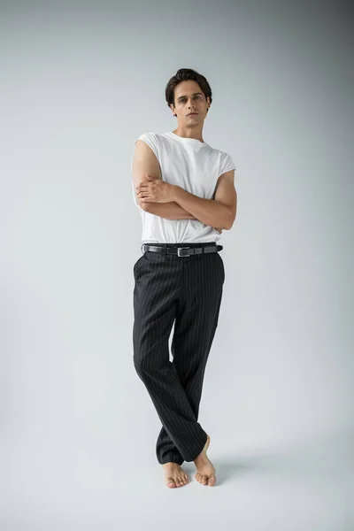 Full length of barefoot man in striped trousers and white t-shirt posing with crossed arms on grey — Stock Photo