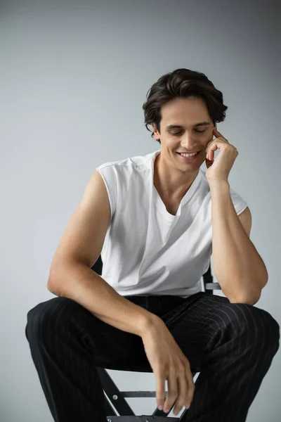 Happy man in striped trousers and white t-shirt sitting on camp chair on grey — Stock Photo