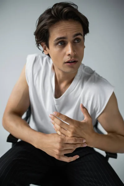 Brunette homme en t-shirt blanc élégant et pantalon regardant loin tout en posant sur gris — Photo de stock