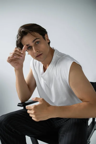 Brunette man in stylish white t-shirt and pants looking at camera while posing on grey — Stock Photo