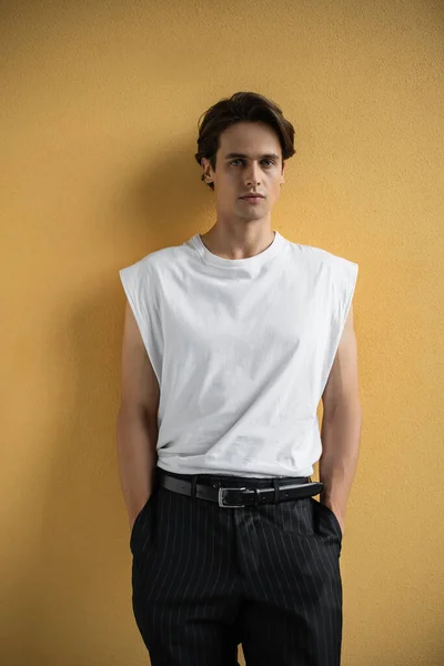 Hombre con estilo en camiseta blanca y pantalones a rayas de pie cerca de la pared amarilla - foto de stock