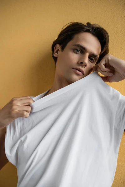 Stylish man adjusting white t-shirt and posing near yellow wall — Stock Photo