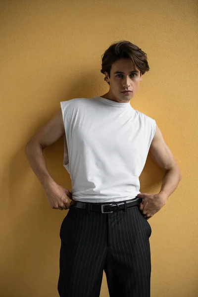 Stylish man in white t-shirt and striped pants standing near yellow wall — Stock Photo